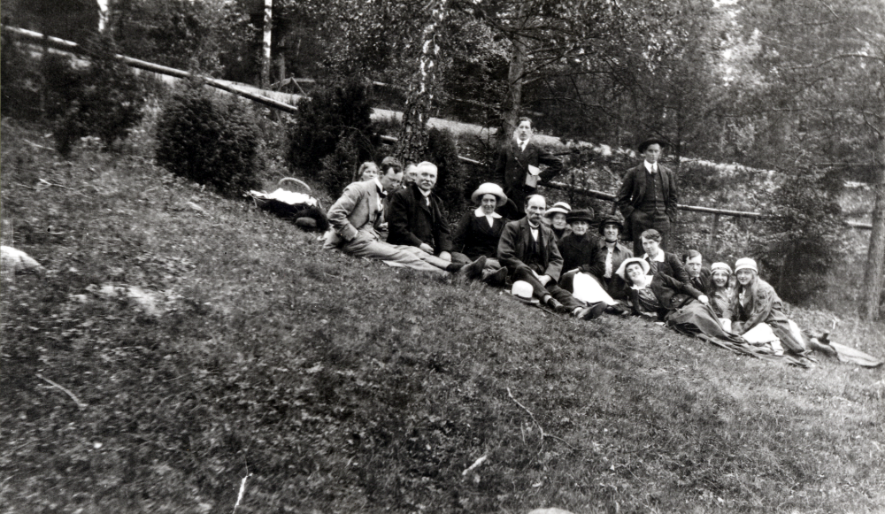 Utflykt i det gröna med utsikt över Vallentunasjön.  Kaffekorgen är packad och man sitter i slänten vid gamla järnvägsövergången norr om Bällsta.  Fr v Hjalmar Torell, Berna  och Henning Henningsson, P F Torell, okänd, Erik Torell, ? Fredriksson, okänd, okänd, Lisa Lundgren, okänd, Rut Torell, okänd, okänd, okänd och okänd