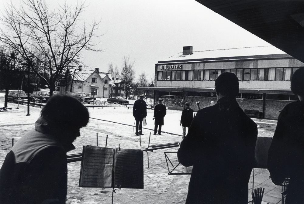 Sveriges arbetareparti m fl socialistiska partier i Vallentuna ordnar första maj-demonstration med samling bakom Centrumbio för att tåga till Tuna torg. Det är snöglop och slaskigt. På torget står endast ett par stycken åhörare