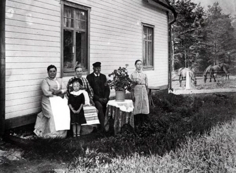 Familj som står och sitter framför ett hus