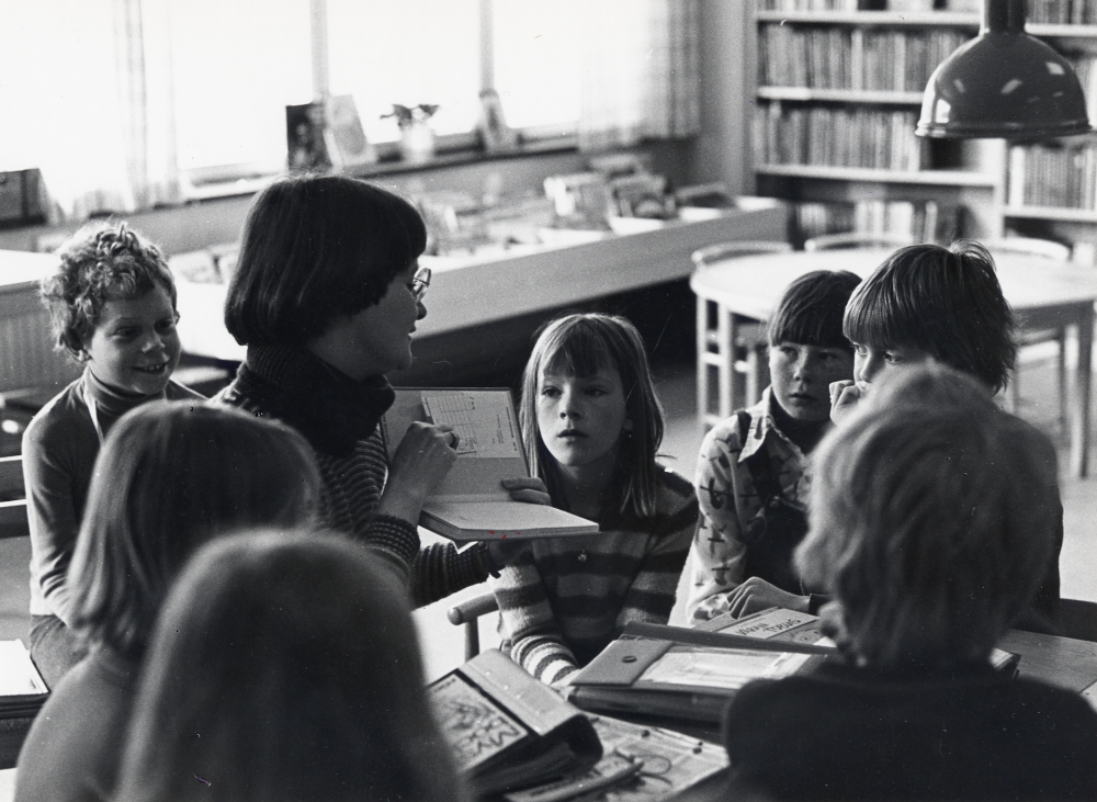 Ann Davidson har besök i Vallentuna bibliotek i barnavdelningen av skolans årskurs 3 och informerar om biblioteket. Biblioteket låg 1 trappa upp ovanför Konsum, nuvarande Torghuset