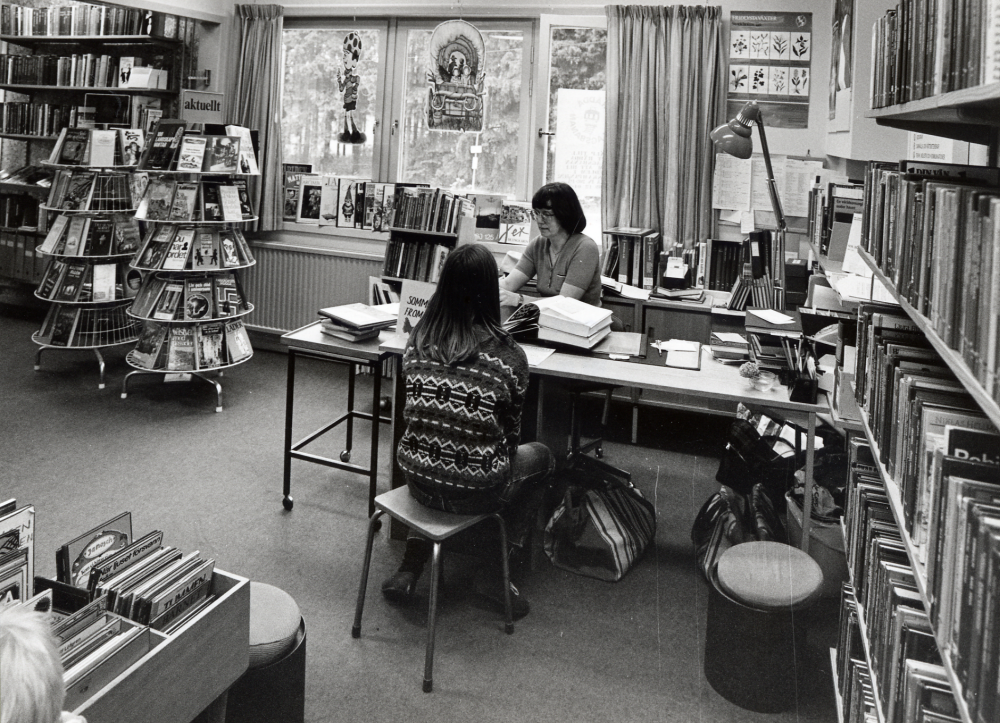 Kårsta bibliotek i stationshuset vid Kårsta järnvägsstation. Snart skall biblioteket flytta till nya Kårstaskolan vid Bergsjövägen och bli ett integrerat skol- och folkbibliotek. Vid disken sitter bibliotekarien Ulla-Britt Kvarnestam. Ulla-Britt tillträdde tjänsten som filialföreståndare i Kårsta 1 november 1976