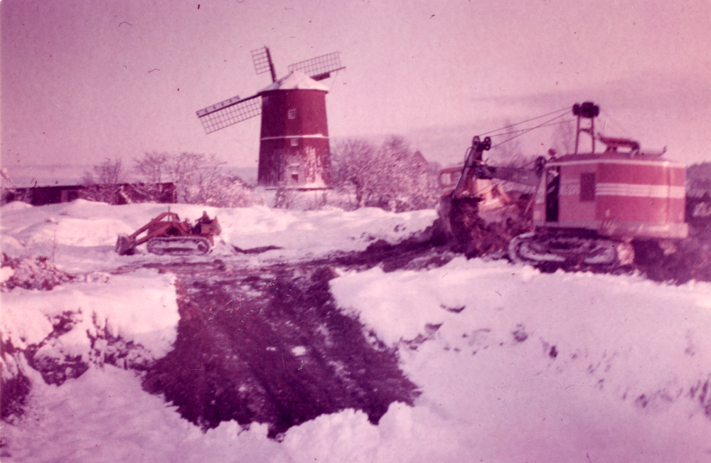 Kvarnbadet – friluftsbad med tre bassänger, uppfördes intill Väsby kvarn och invigdes sommaren 1970. Här syns anläggningsarbete för det nya badet. T v syns ladygården vid Vallentuna prästgård och i bildens mitt Väsby kvarn med en vinge skadad efter en storm i oktober 1969. Arbete med en caterpilar och en grävskopa pågår.
