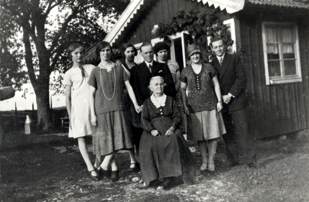 Tekla Johansson sitter med släkt och vänner utanför Oppgården i Kragsta.  De mörka kvinnorna t v om Tekla är döttrarna Anna och Märta.

Uppgift om fotoår saknas.