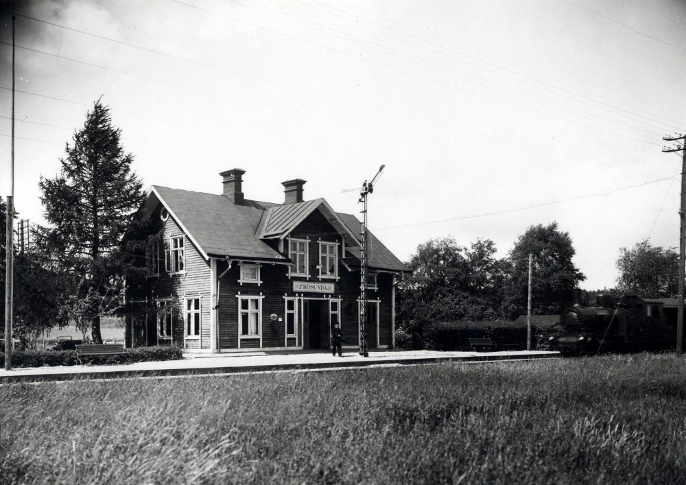 Frösunda järnvägsstation. Ett ånglok kommer in på stationen.  Sefamoren visar infarten klar.  På perrongen står en uniformsklädd person, Siri Wallerstdts far?
2021-01-13: Fotograferad efter 1940 enligt Järnvägsmuseets uppgifter