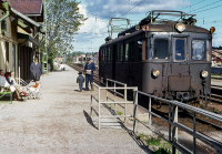 Vid Vallentuna station. Ett tåg har stannat vid stationen, konduktören står på perrongen och pratar med en litet barn. Väntande resenärer sitter på en bänk framför stationshuset.
Bildserie: Vallentuna på 1960-talet.