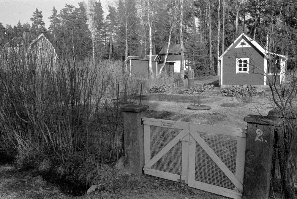 Bebyggelse och natur vid Fågelsångsvägen i Kristineberg innan husen revs och området röjdes inför byggstarten av Arningeleden. På grinden står namn och adress, Valter Karlsson Fågelsångsvägen 2.