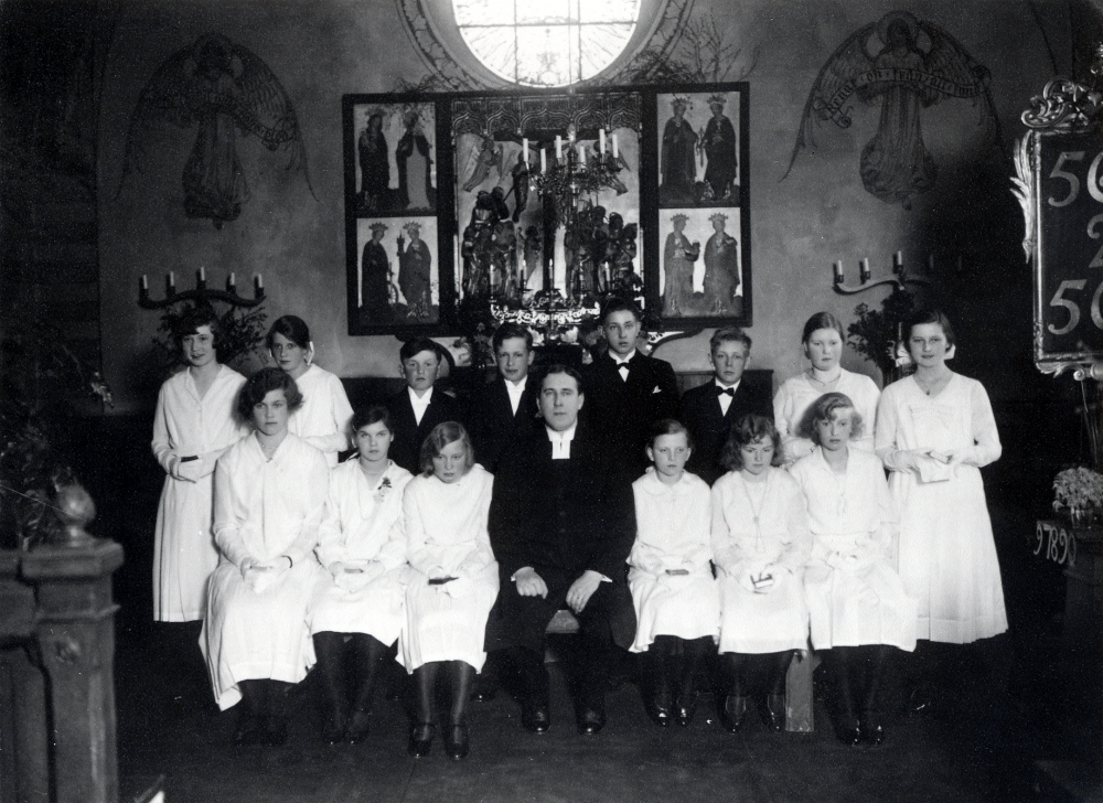 Konfirmation i Frösunda kyrka. Vid altaret står i övre raden fr v Svea Johansson, Naimi Lundkvist, Gustaf Jansson (Thoreaus), Karl Erik Helgöstam, Sven Wredh, Henry Roos, Hillevi Larsson och Sonja Fundell. Sittande fr v Dagny Lundgren, okänd, Maj Åkerlind, kyrkoherde Paul Sjöberg, Ella Stolpe, Gulli Grandin och Elsa Ekberg