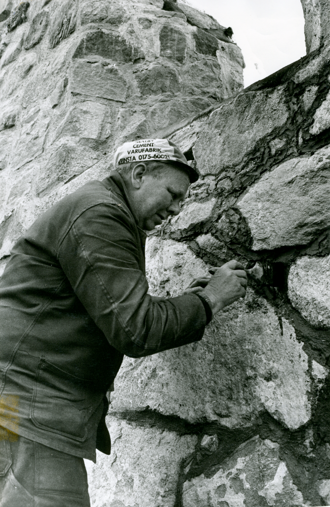 Arne Holm utför restaureringsarbetet vid kyrkoruinen i Brottby.

Össeby kyrka ödelades 1838 efter sammanslagning av Össeby och Garns socknar. Taket till kyrkan brann efter ett åskväder 1856 och byggnaden förföll sedan alltmer. 1961 startade Össeby hembygdsförening ett restaureringsarbete och 1976 invigdes ruinen som kyrkorum för friluftsgudstjänster, konserter, dop och vigslar.

•Fotografiet ingår i bildserien ”Vardagsliv i Vallentuna kommun” av Rachael Gough-Azmier & Gunilla Blomé, Haga Studios HB.