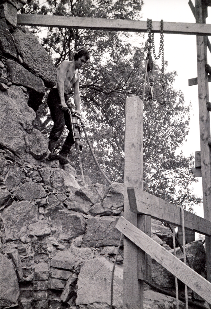 Roland de Thorest de Thorey, den drivande kraften bakom restaureringsarbetet av Össeby kyrkoruin, borrar i muren på sakristians gavel. För att förankra de löst liggande stenarna borrades spett ner i murlivet vilka därefter förankrades upptill med järnkrampor. En kappa göts därefter över som sedan målades med tjära.