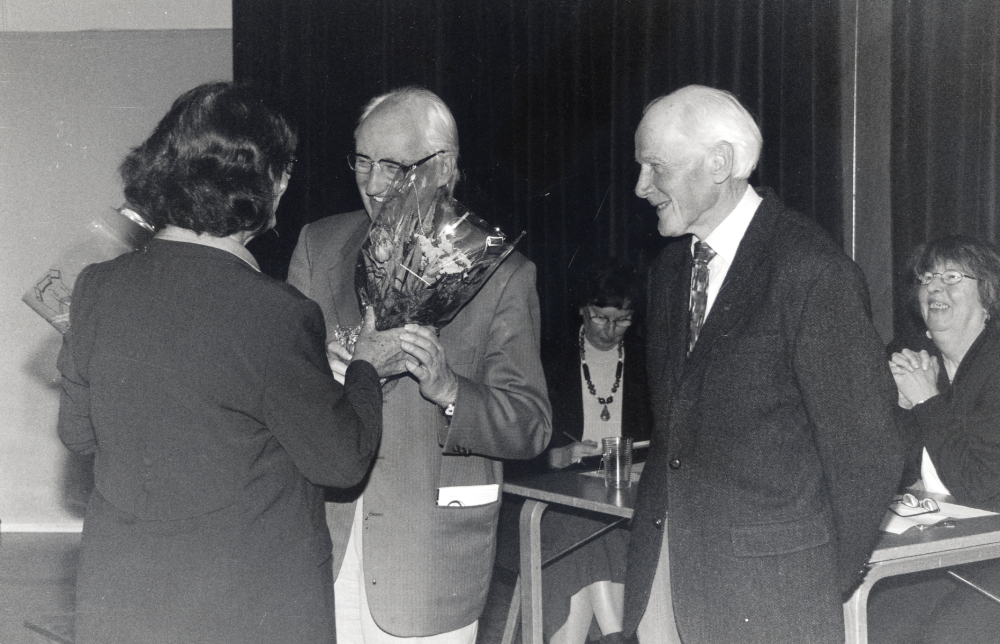 Vallentuna biblioteks vänner har årsmöte och 10-årsjubileum i Vallentunasalen.  Marianne Diedrich överlämnar blommor till Karl-Axel Elmquist, vald till ordförande på årsmötet 2000, men drabbades av sjukdom och  kunde inte arbeta under valperioden.  Gunnar Käller väntar på sin tur och avtackas efter att ha varit vännernas kassör för starten för tio år sedan