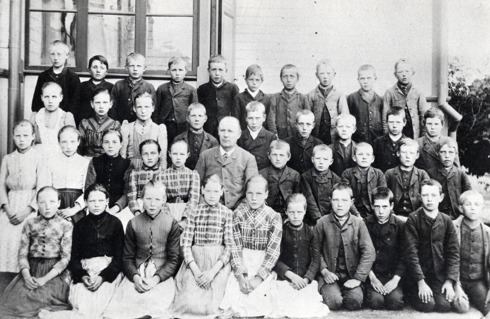 Läraren och organisten C A Carlsson tillsammans med skolbarnen i Össeby-Garns kyrkskola.  Syskonen Kraemer finns med på bilden.  C A Carlsson bodde i Gustafsberg, Össeby-Garn.

Uppgift om fotoår saknas, men troligen början av 1900-talet.