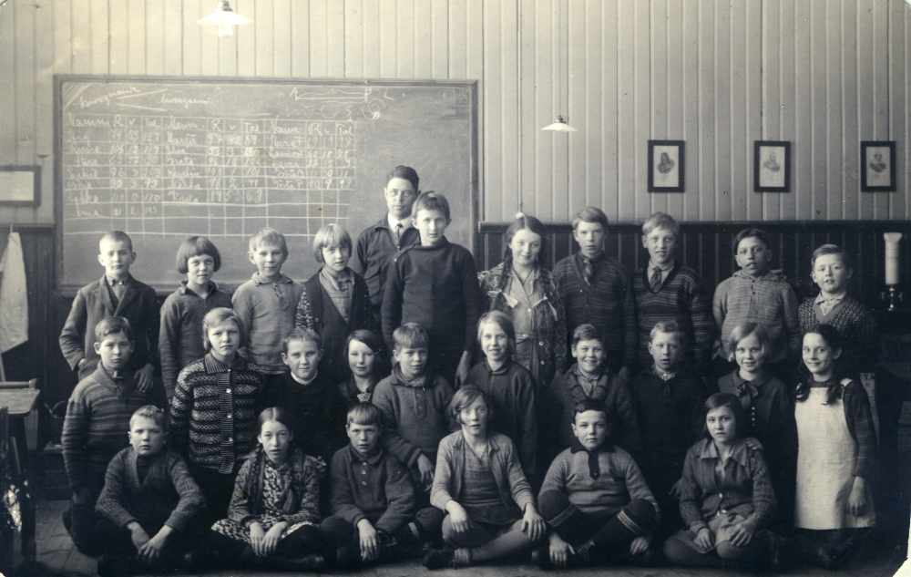 I ett av klassrummen i röda skolan står läraren Josef Andersson med sina elever. Nummer fyra från vänster i mellersta raden är Märta Eriksson (gift Bergqvist).