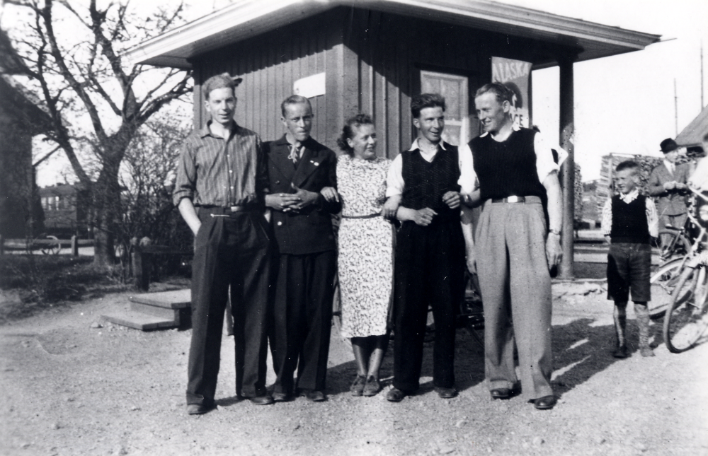 Söder om Vallentuna järnvägsstation fanns en kiosk.  Där samlades ungdomarna fr v Sven Nordgren, Lennart Johansson, Ulla Gustafsson, Edvin Nordgren och Nore Andersson.  T v syns gaveln på stationshuset där en järnvägsvagn står vid perrongen.  T h om kiosken syns även godsvagnar lastade med ved.  På kiosken sitter en skylt med Alaska-glace