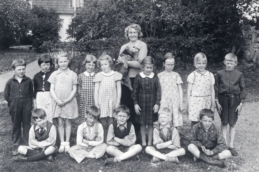 Lärarinnan  Valborg Wallin-Eriksson  tillsammans med skolbarnen i 1 och 2 klass vid  Orkesta småskola  I famnen har hon en  hund  Fr v bakre raden:  Herman Lindkvist   Maj-Britt Jansson   Rosa Åhlén   Gurli Larsson   Gerd Forsberg   Kerstin Rosén   Anna-Greta Lundkvist   Ulla Åhlén  och  Karl-Erik Jansson  Främre raden fr v:  Folke Thunberg   Bert Lindström   Sivert Karlsson   Lennart Jansson  och  Arne Lundkvist   Uppgifter: Bert Lindström