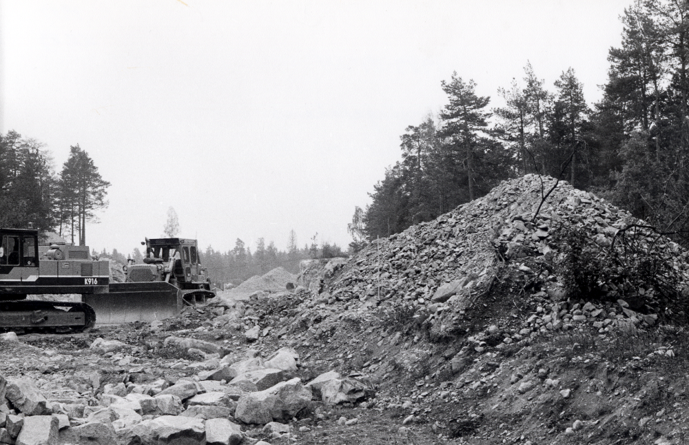 Arningeledens anslutning till Angarnsvägen byggs och bekostas av Vallentuna kommun för att förmå Vägverket att bygga hela leden och därigenom minska biltrafiken genom Täby kyrkby.  Kraftiga maskiner med larvfötter  och schaktblad arbetar i stenhögarna.