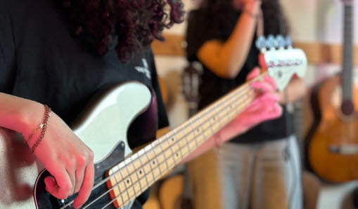 barn i mellanstadieåldern sitter glada tillsammans och håller upp olika sorters instrument, mestadels gitarrer.