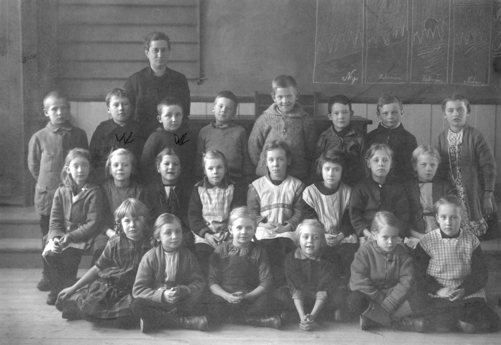 Lärarinnan Anna Gauffin tillsammans med skolbarnen inne i skolsalen i Hjälmsta skola. I mittenraden nr 3 fr v sitter Maj Linder