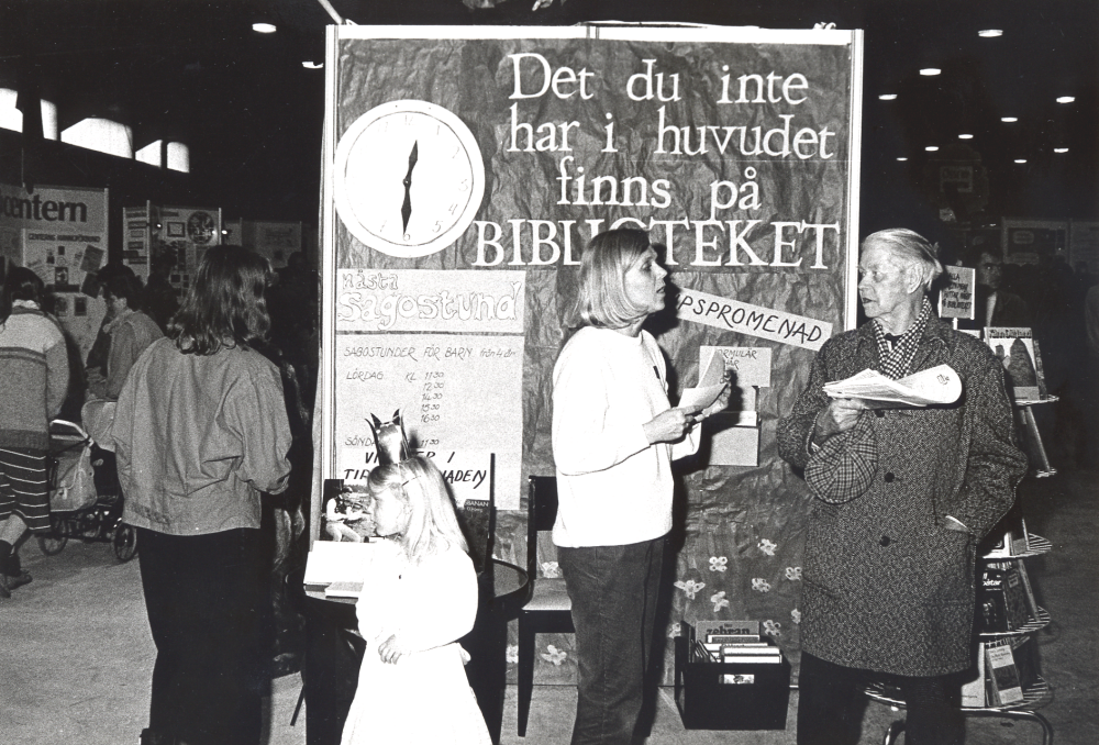 Vid Föreningarnas festival i Vallentuna ishall 19-21 april 1986 fick föreningar och kommun presentera sin verksamhet med utställningar, sång och musik. Här syns Vallentuna biblioteks monter byggd som en bokbuss med sagogrotta. Här samtalar kulturchef Ingrid Ullman med Josef Andersson vid bussens gavel. Den lilla prinsessan är Sara Ullman .
