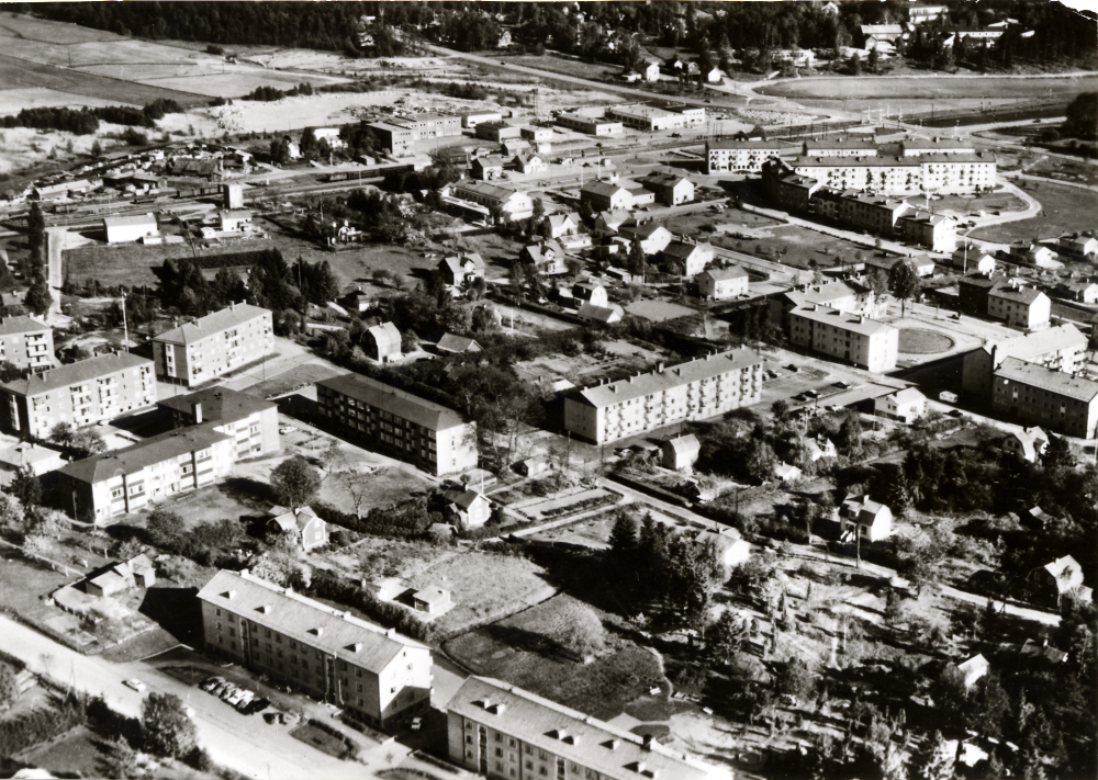 Flygfoto över Vallentuna centrala delar. I bakgrunden fr v, Vallentuna såg, Maskin-Tellus och Vallentuna motor. Längst till höger den nygjorda Angarnsvägen och från   järnvägskorsningen t v Vallentuna järnvägsstation och Vallentuna järnvägshotell Flugan. Framför stationsområdet ligger nya Konsum, ännu ej färdigbyggt. I förgrunden flerfamiljshus på Fornminnesvägen