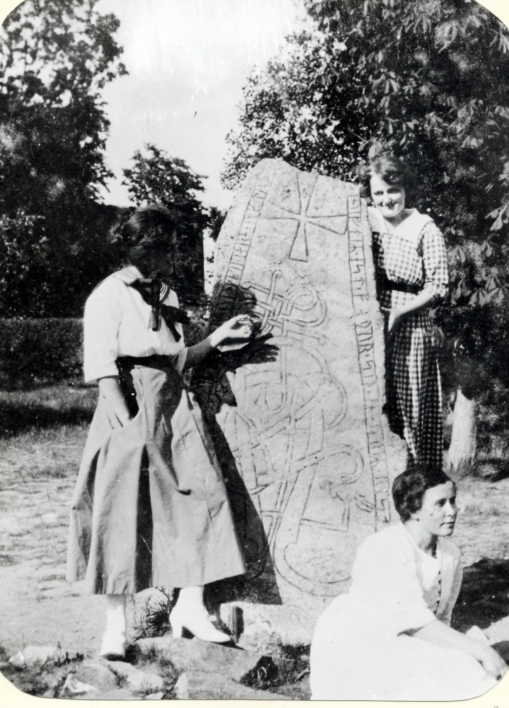 Linnea och Viola Åslev vid runstenen utanför Össeby-Garns kyrka.  Flickorna har hälsat på hos barnmorskan Selma Gustavsson som bodde i kyrkskolan. Det är Selma som sittter vid runstenens fot.  Flickorna Åslev var döttrar till kyrkoherde Per Erik Åslev