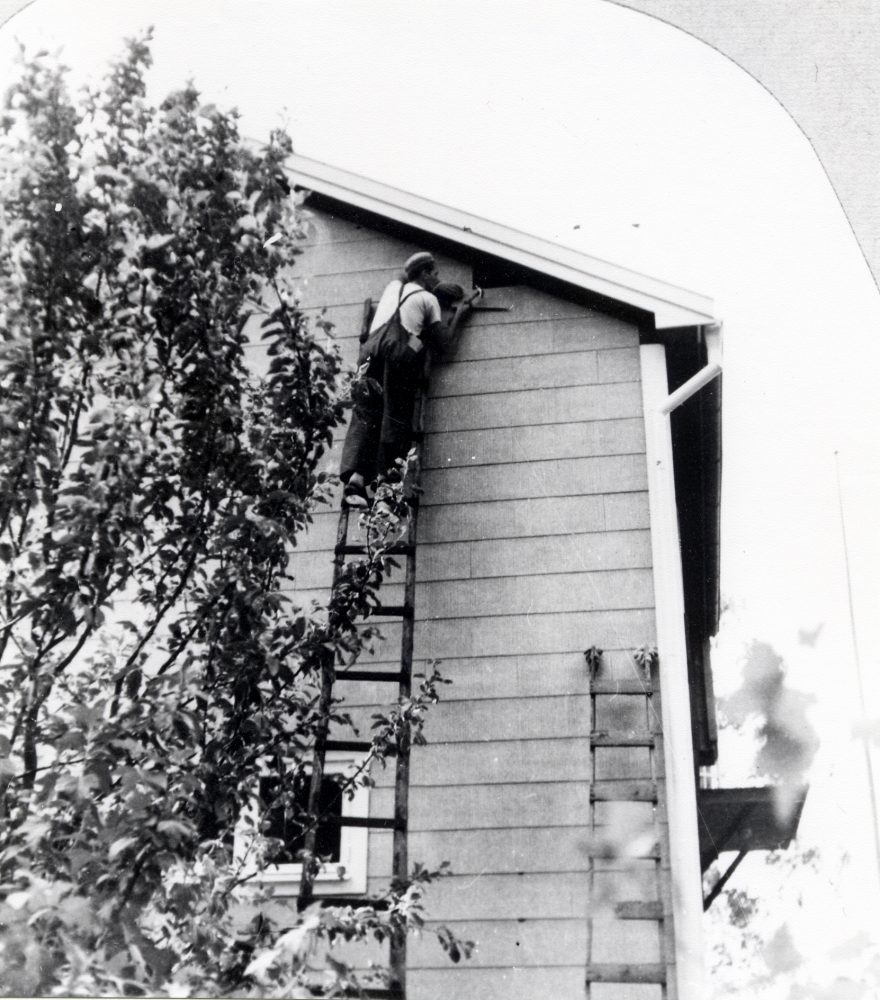 Erland Rost sätter fast sista beige-gula eternitplattan på huset Högbo, med nuvarande adress Klingspors väg 6.  Erland Rosts svärföräldrar Helen och Hans (Johannes) Hammar köpte huset 1938 som sommarbostad, då kallat Högbo.  Det blev senare  familjen Rosts hem och 1989 hade huset samma beklädnad.  Det stora trädet är ett åkeröträd