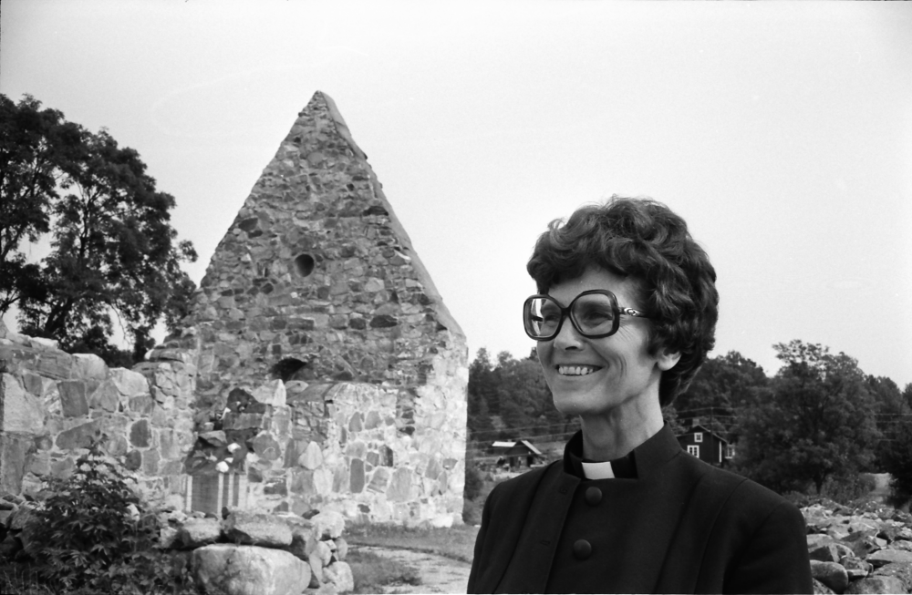 Inga-Britt Lindell, ny kyrkoherde i Össeby-Garn, fotograferas utanför Össeby kyrkoruin. 
•Fotografiet ingår i bildserien ”Vardagsliv i Vallentuna kommun” av Rachael Gough-Azmier & Gunilla Blomé, Haga Studios HB.
