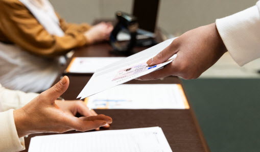 En person räcker över valkuvert till sittande röstmottagare.