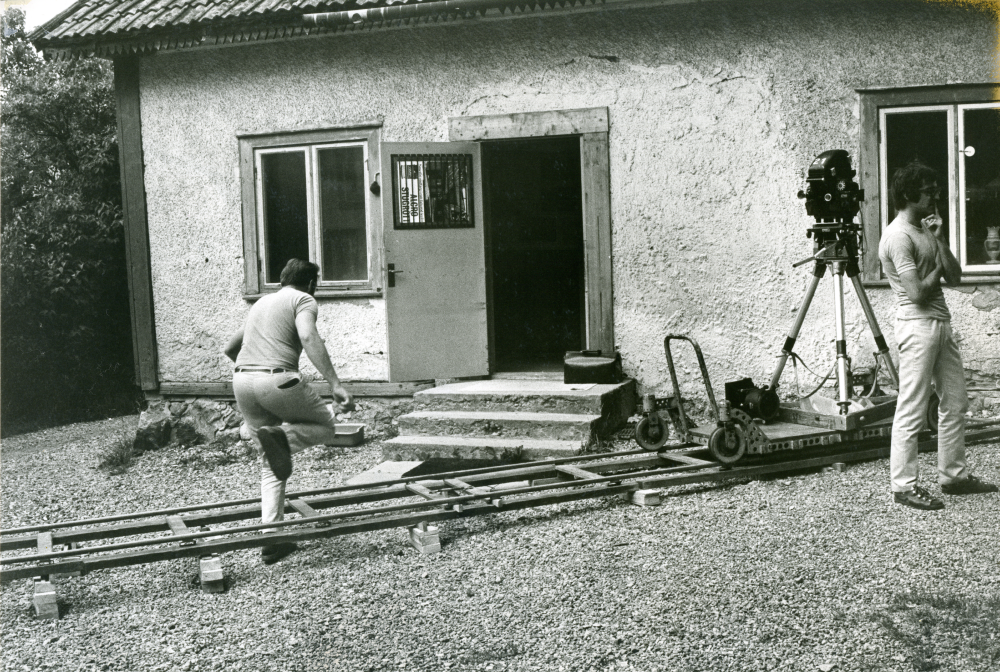 Filminspelning på Åbyholms gård. Regissören Jiri Tirl, till höger i bild, spelar in en scen hos antikvitetshandlare Sten Zetterlund på Åbyholms gård den 11 juli 1973. Zetterlund tar ett kliv över rälsen med filmkameran, på väg mot ingången till norra flygeln.
•Fotografiet ingår i bildserien ”Vardagsliv i Vallentuna kommun” av Rachael Gough-Azmier & Gunilla Blomé, Haga Studios HB.