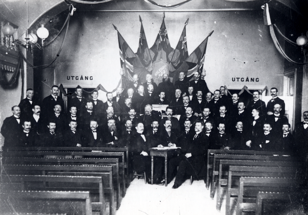 Nykterhetsföreningen Blå bandet har konferens i Stockholm. I talarstolen med skägg står Jakob Byström, dåtidens framstående riksdagsman, även verksam inom Blå bandet och redaktör för Veckoposten