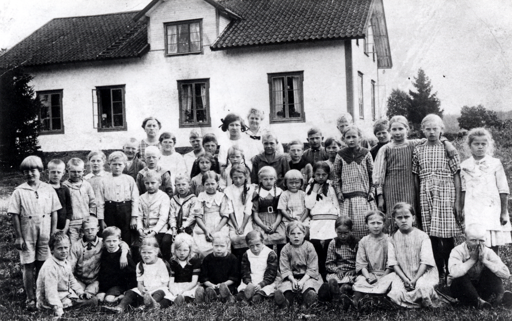 Lärarinnan Lydia Persson i rutig klänning och lärarinnan Gerda Wikland i ljusa kläder tillsammans med skolbarnen utanför Stångberga skola.  Stående i bakre raden är fr v Gustaf Adolf af Ekenstam, okänd, okänd, Gurli Ahlén, Georg Johansson, okänd, Valter Rödin, Kerstin Gustavsson Sture af Ekenstam, Astrid Ahlén, Alf Skålberg, Hebbe Gustavsson, Dagny Karlsson, okänd, Mattias Lien, Georg Andersson, Gulli Hedman, Lennart Rödin, Jenny Nyström, okänd, Greta Rödin, Signe Lundgren och Betty Boman.  Sittande i mitten mellan de stående  fr v Erland Fransson, Janne Sundgren?, Ragnhild Ekman, Valborg Karlsson,  Elisabeth (Lisa) Lundgren, Stig Persson och Eva Sundgren.  Sittande i gräset fr v okänd, okänd, okänd, Linnea Ahlén, Elsa Rödin, Gudrun Lien, Ingeborg ?, Margit Johansson, Karin Nyström, Elin Lien, Ebba Fransson och Olle Mattsson