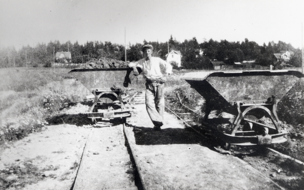 Harry Andersson arbetade vid Åby tegelbruk.  Här står han vid två av de vagnar som gick på en decauvillejärnväg.  Vagnarna användes för transport av lera till tegelbruket