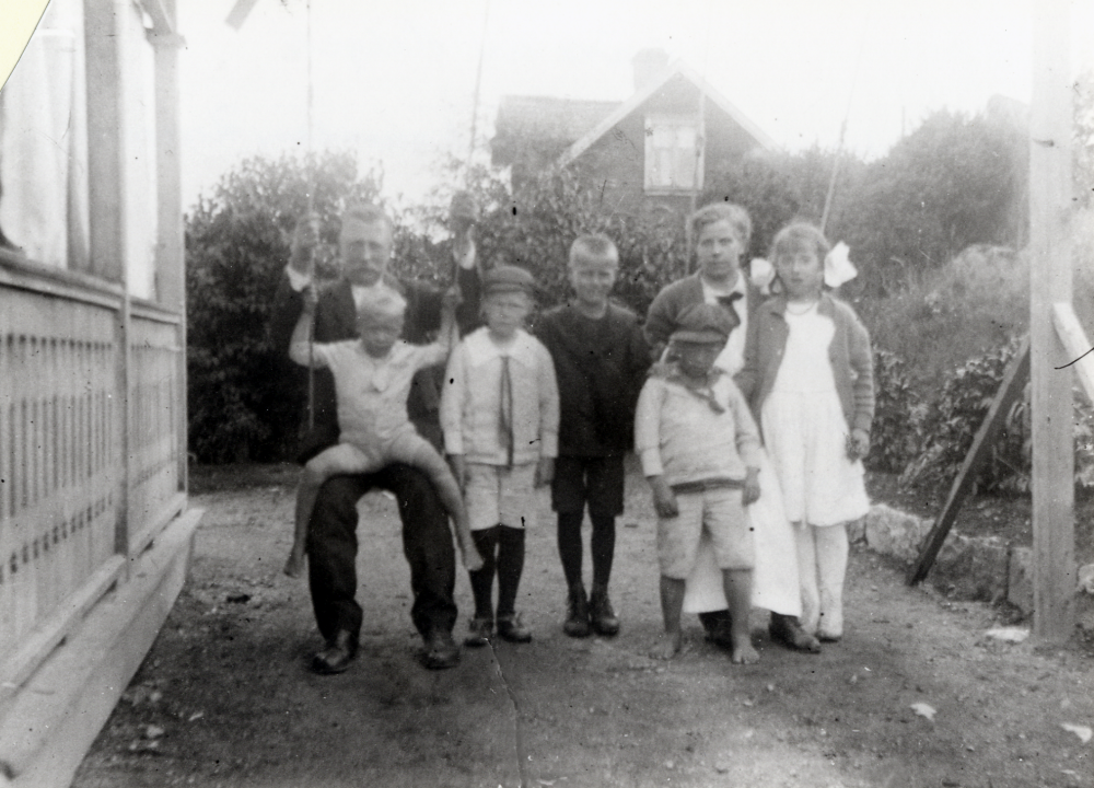 Henning Henningsson med barn och sommargäster vid Klippan på Banvägen.  På gungan sitter Henning med Karl Axel Cassel i knäet, bredvid fr v står sönerna Stig, Helge och Bernhard samt fru Drews och Karin Drews.  Familjen Drews hyrde av Henningssons.  I bakgrunden syns vila Rosenhill