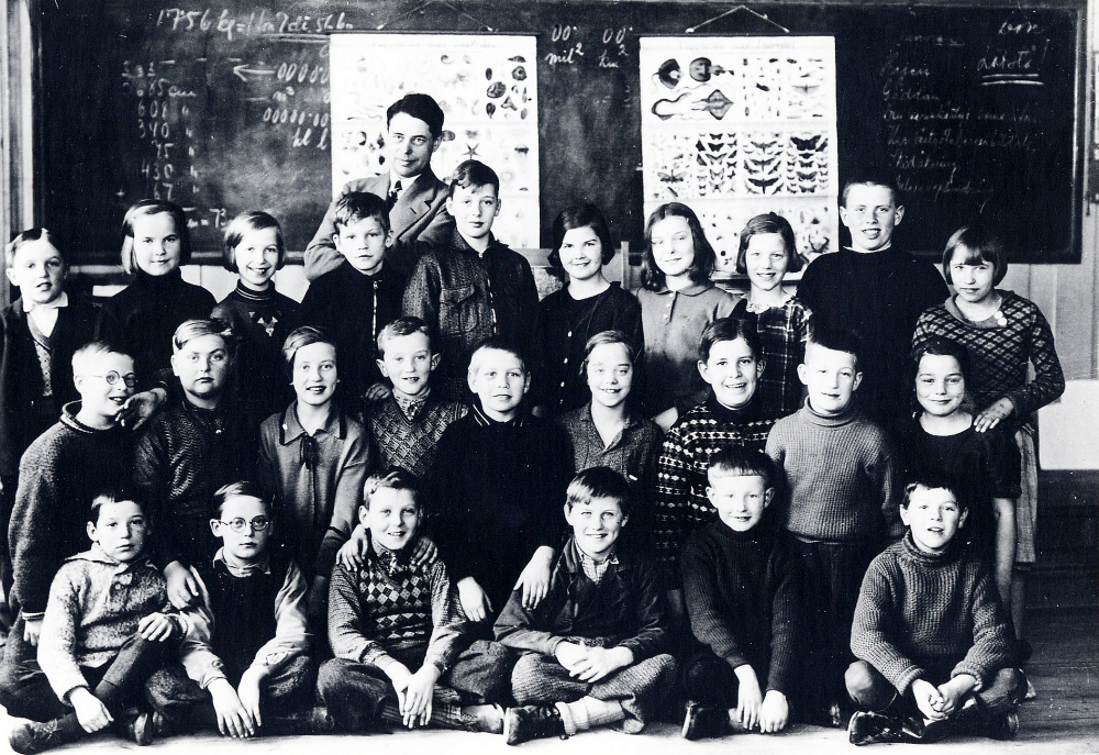 Interiör från Röda skolan i Hjälmsta skola. Läraren Josef Andersson tillsammans med klass 4. Övre raden fr v Erik Sköld, Nancy Andersson, Birgitta Öberg, Hadar Johansson, Erik Geijer, Linnea Hedin, Arny Bengtsson, Maj Frösling, Herbert Larsson, och Sigrid Forslund. Mellanraden fr v Bertil Hansson, Rune Jansson, Dagny Wallberg, Lennart Bergström, Josef Olsson, Märta Karlsson, Per Lengquist, Gustav Grandin och Ulla Kjörling. Nedre raden fr v Sigvard Andersson, Olle Karlsson, Bengt Lindgren, Vide Jansson, Bror Andersson och Stig Eriksson