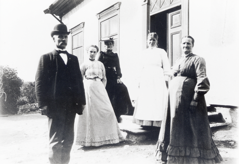 Folkskolläraren Per Ferdinand Torell tjänstgjorde i Vallentuna 1887-1919. Här står han utanför Klockargården , som var både skollokal och bostad, tillsammans med sin dotter Kerstin Torell gift Westerlund i rutig klänning och längst t h hustrun Hanna Torell. Uppgifter från Torells dotterson Egon Westerlund. Kvinnan i vita kläder är Berna, född Rundstedt, nyanställd barnmorska i Vallentuna socken, 1910 gift med Henning Henningsson