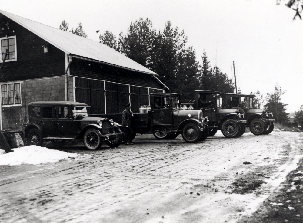 Bilar utanför Helge Anderssons garage i Skrattbacken, Markim.  Helge Andersson drev lastbilsrörelse i  Markim. Han överlät rörelsen till Roslagsbanans järnvägar som startade  Roslagsbanans lastbilsstation i Markim.  Fr v står Helge Anderssons personbil Hauptmobile, lastbilen Tidaholm med chauffören Gustaf Andersson och Helge Andersson, som lutar sig mot bilens flak. Bilens dörr är märkt med Roslagsbanans SRJ.    De två övriga lastbilarna är av märket Garford.  Chaufförerna har inte kunnat identifieras