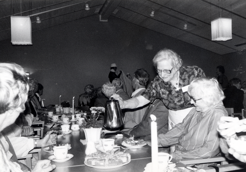 Pensionärsföreningen KOM har modevisning i Mathiasgården. Kläder från Ceci, Mamsell Kerstin och Björns herrmode visades av egna mannekänger. Accessoarer från Rosita.  Inträde 25 kr. KOM bjöd på kaffe, smörgåsar och ambrosiatårta. Här serverar Rut Ekstedt Anna-Lisa Plick kaffe. På scenen visar Margareta Selander hatt, kappa och klänning