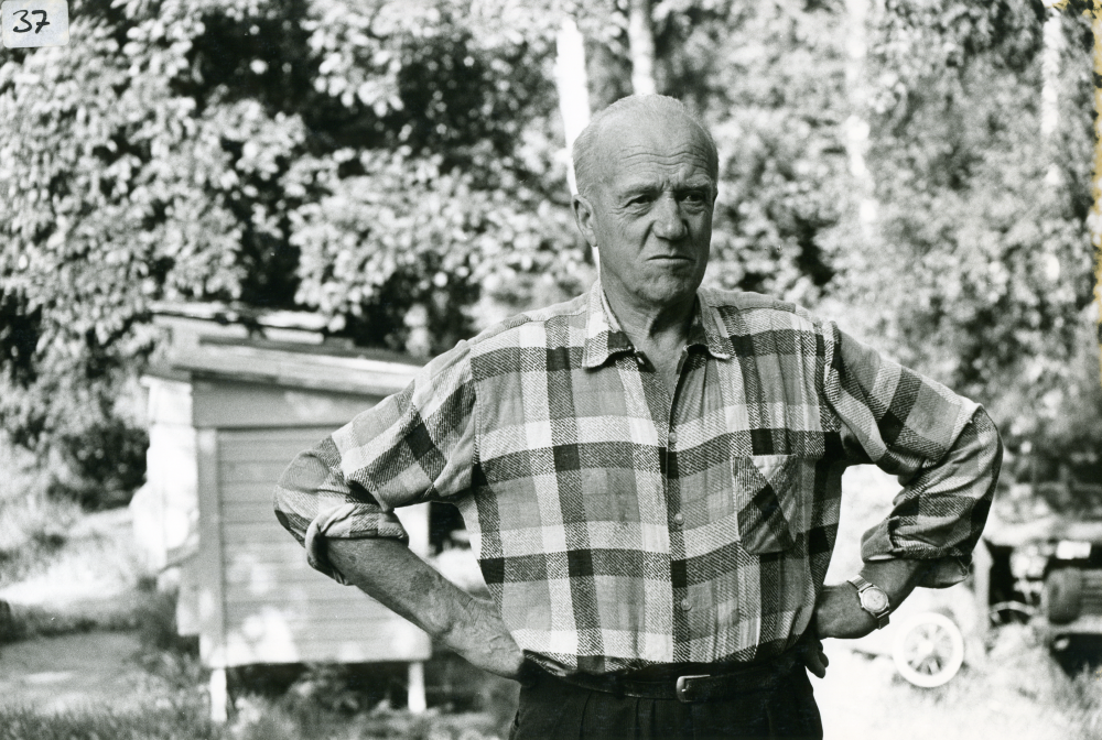 Biodlare Thitus Hahn på Åbyholmsvägen i Vallentuna. I bakgrunden syns bikuporna som står på rad i trädgården. Thitus Hahn var tidigare trävaruhandlare.
•Fotografiet ingår i bildserien ”Vardagsliv i Vallentuna kommun” av Rachael Gough-Azmier & Gunilla Blomé, Haga Studios HB.