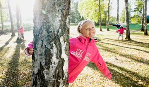Flicka som står bakom ett träd på skolgården