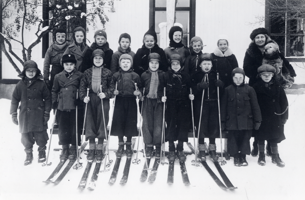 Lärarinnan Valborg Wallin-Eriksson tillsammans med skolbarnen i 1 och 2 klass utanför Orkesta småskola. I famnen har hon sin hund. En del av barnen har skidor. Övre raden fr v Lennart Jansson, Berit Karlsson, Ulla Öhman, Inga Åhlén, Karin Rosén Bäckman, Daisy Nilsson, Gerd Lindström Magnusson och Ulla Britt?. Nedre raden fr v Hilding Jansson, Hilding Andersson, Sven Hammarstedt, Melker Lundkvist, Stig Hammarstedt, Börje Thunberg, Sture Björklund, Bernt Lundkvist och Bengt Jansson