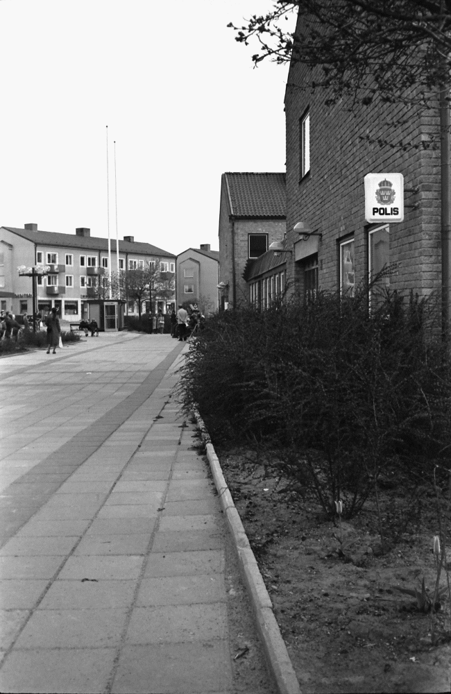 Polisens skylt på fasaden på gamla kommunalhuset. I bakgrunden till vänster syns flerfamiljshusen på Centralvägen.
•Fotografiet ingår i bildserien ”Vardagsliv i Vallentuna kommun” av Rachael Gough-Azmier & Gunilla Blomé, Haga Studios HB.
