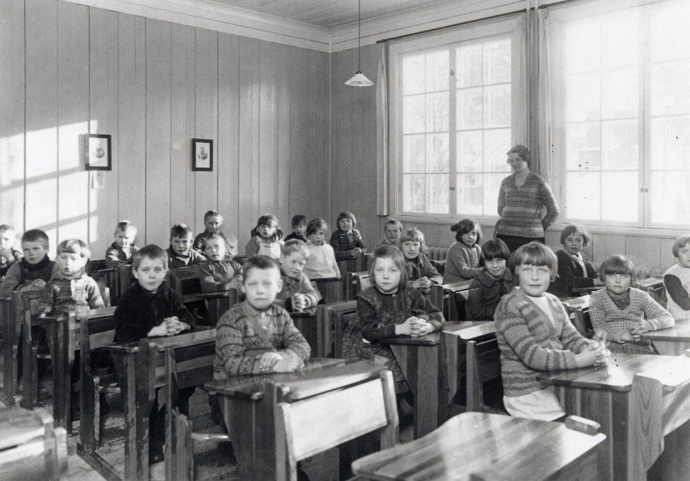 Lärarinnan Margit Oppermann tillsammans med barnen i klassrummet i Röda skolan i Hjälmsta. I raden närmast kameran sitter fr v okänd, Åke Karlsson Solgården, okänd, okänd och Bengt Edman. Rad 2 fr v okänd, Tage Andersson Nyhaga, okänd, Reinhold ?, Mary Karlsson och Mary Lejholm. Rad 3 fr v okänd, okänd, Lilly Jansson Kragstalund, Inga Elisabet Andersson Hygel Byle, Anne-Marie Broman, och Astrid ? Lövsättra. Rad 4 närmast fönstret fr v v okänd, okänd, okänd, Ingrid Dannemann, Annie Jansson Kragsta och Ingrid Jansson