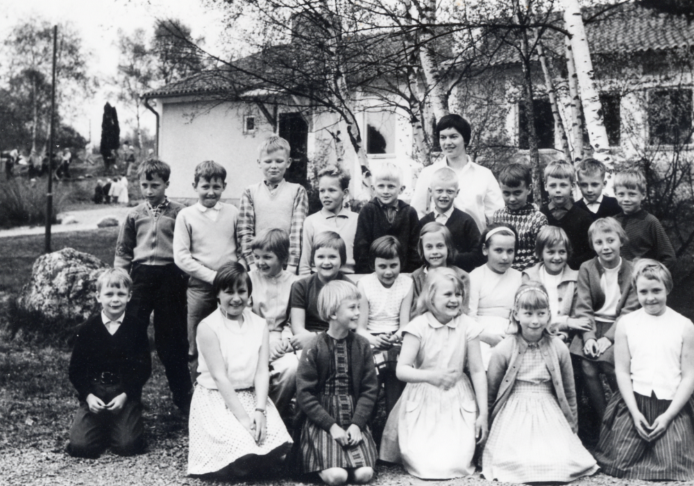 Lärarinnan Britt Ohlsson tillsammans med skolbarnen i Hjälmsta skola i lågstadiet.  Fr v i översta raden nr 3 Magnus Rost,  nr 4 Kent Gustafsson, nr 6 Billy Jägborn, nr 7 Peter Åberg.. Mellanraden fr v nr 5 Kerstin Blomberg, Yvonne Åkerman okänd placering. Knästående fr v nr 1 Johan Ek, numera Grill, nr 2 Lena Johansson och nr 4 Agneta Jansson