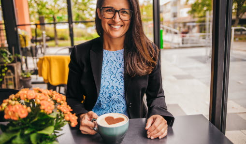 Leende kvinna sitter med kaffekopp i handen.