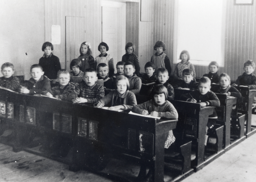 Skolsalen i Orkesta småskola.  I främre raden sitter fr v Karl Gustav Lundkvist, Axel Andersson, Harry Berggren, Helge Öhman, Stina Carlsson och Kerstin Björklund.  Andra raden fr v Hilda Karlsson, Holger Hedlund, Conn Erik Edlund, Allan Lundkvist och Gunnar Häll.  Tredje raden fr v okänd, Göte Karlsson, Bertil Engstrand och Gunnar Karlsson.  Fjärde raden fr v Finn Beckman och Sven Bergfors.  Flickorna vid väggen fr v ?