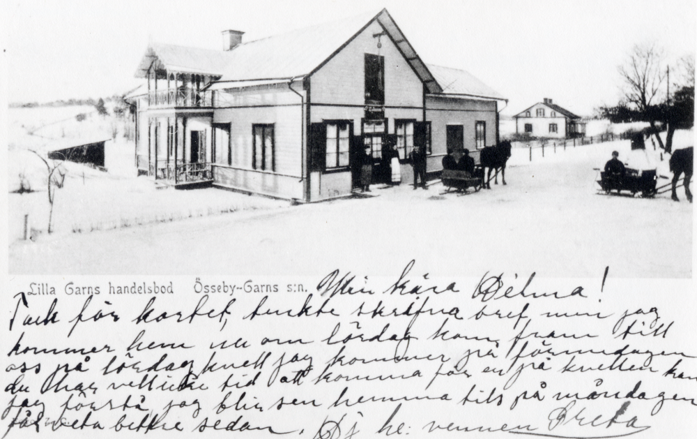 Lilla Garns handelsbod  sedd från  Krukmakarbacken.  Det vita huset  t h är  Klockargården  numera rödmålad. Utanför affären väntar  hästar  med  slädar.  Affären låg i Lilla Garns kyrkby, snett emot Össeby-Garns kyrka