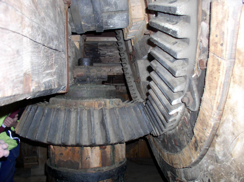 På bilden syns kvarnaxelns ände till höger som överför kraften från vingarna genom ett vinkeldrev till hjärtstocken som syns i bilden mitt. Hjärtstocken driver i sin tur kvarnstenarna.