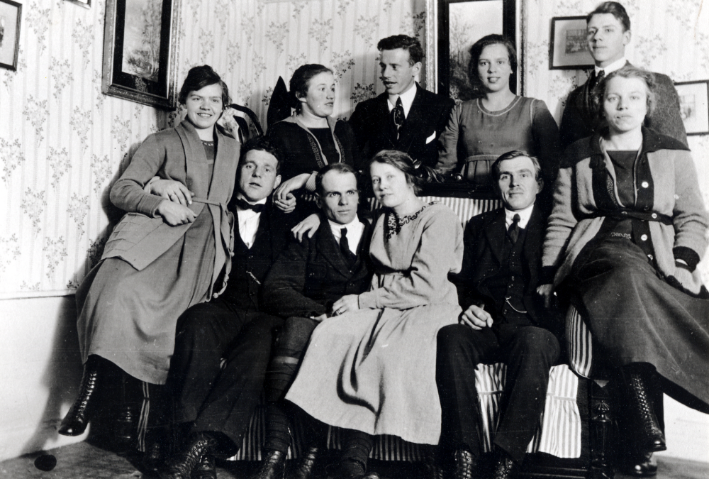 I salen på Helgö gård har ungdomarna samlats. I främre raden sitter fr v Helga Johansson och Holger Céwe som senare gifte sig, Sven Johansson och Edit  som gifte sig och hade Vreda gård, Fritz Andersson och Sally Andersson.  I bakre raden fr v Lilly Höglund, Allan Céwe, Karin Johansson och Gösta Johansson.  Syskonen Johansson antog 1924 släktnamnet Helgöstam
