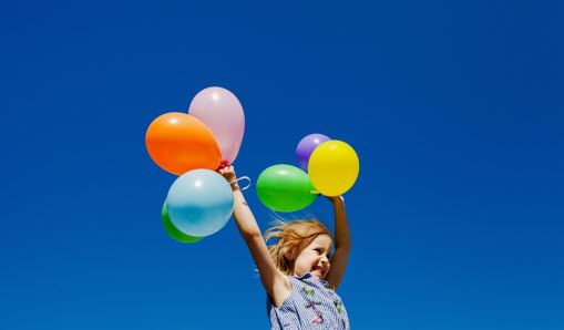 En flicka hoppar i luften och håller i färgglada ballonger.