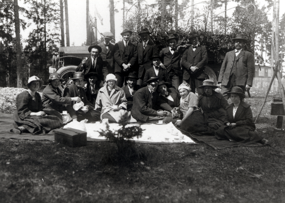 Utflykt till Älvkarleby med Helge Anderssons lastbil av märket Garford med lövat flak, inköpt 1920.  Sittande fr v är Thyra Dahlbeck, Elsa Andersson, dotter till Gottfrid Andersson, Helges hustru Elsa, okänd, okänd, okänd och Helge Andersson själv.  Övriga personer är inte kända.  En kittel/kaffepanna är upphängd över ett primuskök?  En unikabox står framför duken