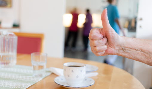 En hand gör tumme upp ovanför en kaffekopp